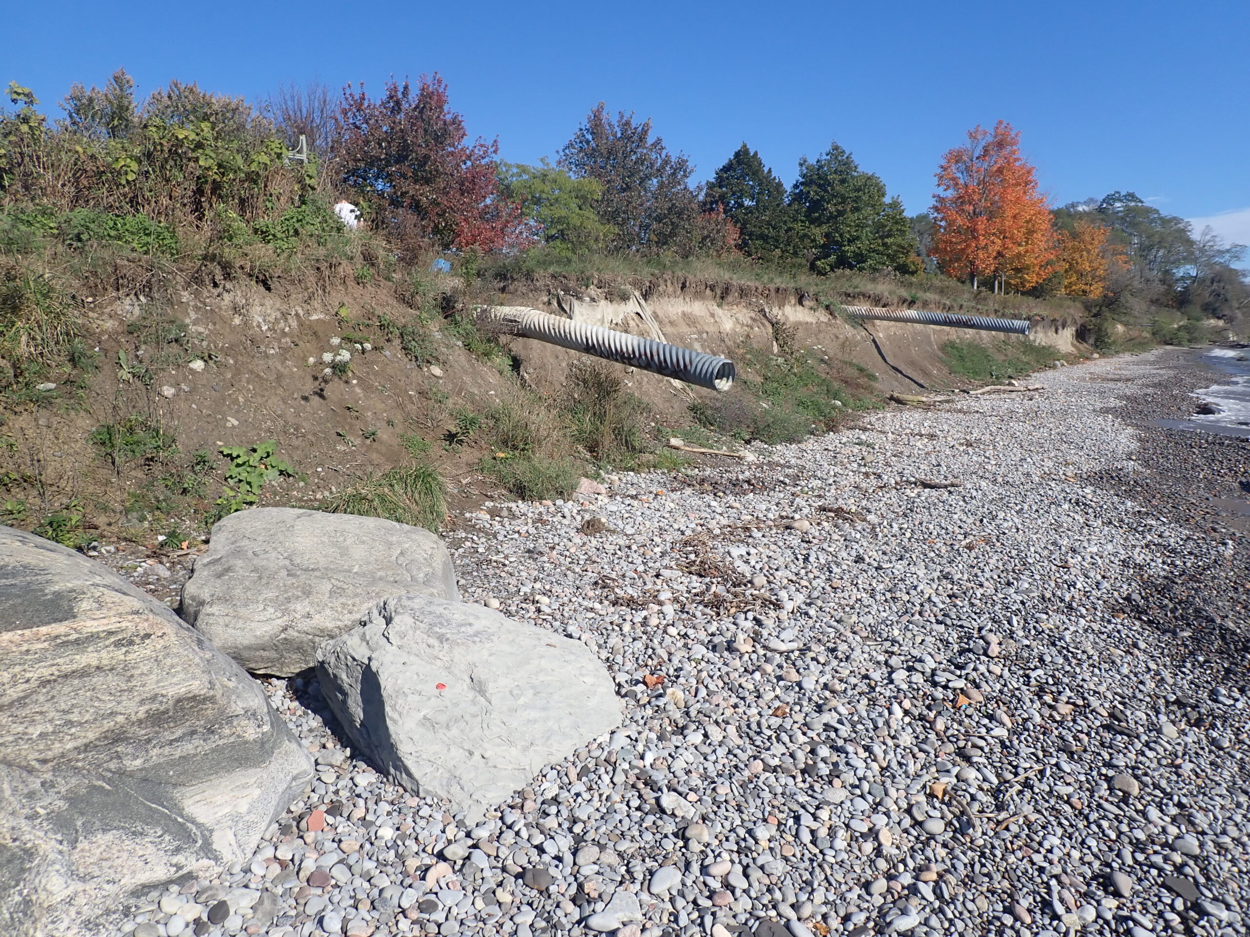A stretch of Ajax shoreline showing rocky beach and eroded bluffs exposing two long drainage pipes.