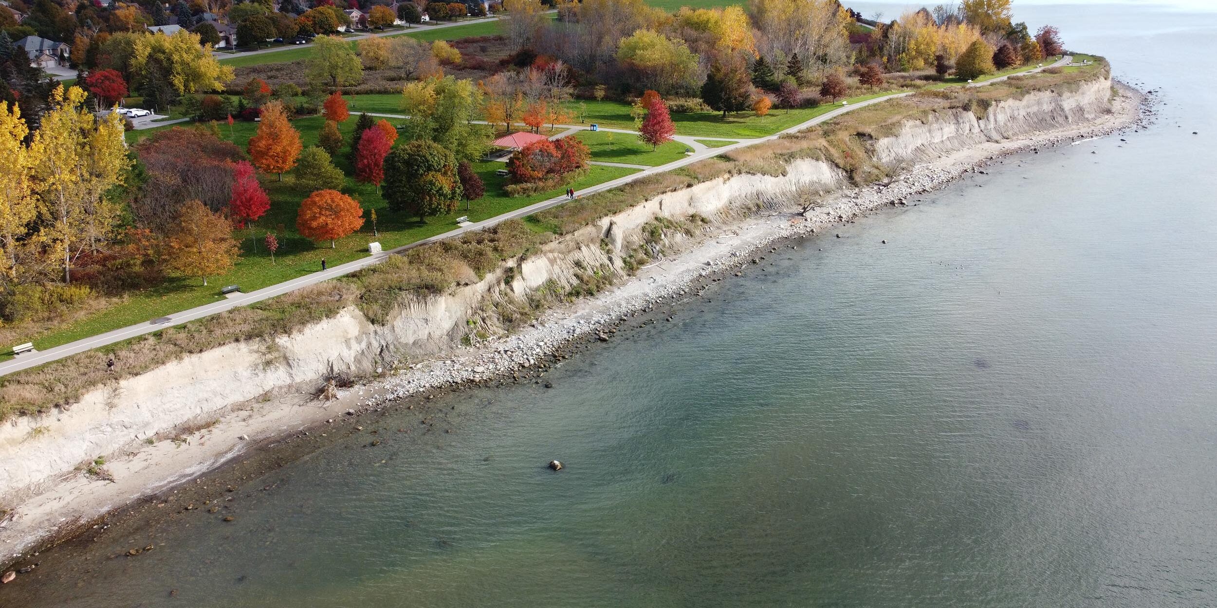 Aerial view of part of Reach 5 facing inland from Lake Ontario showing high, sheer bluffs, a narrow sand beach and a small strip of land between bluffs and Waterfront Trail