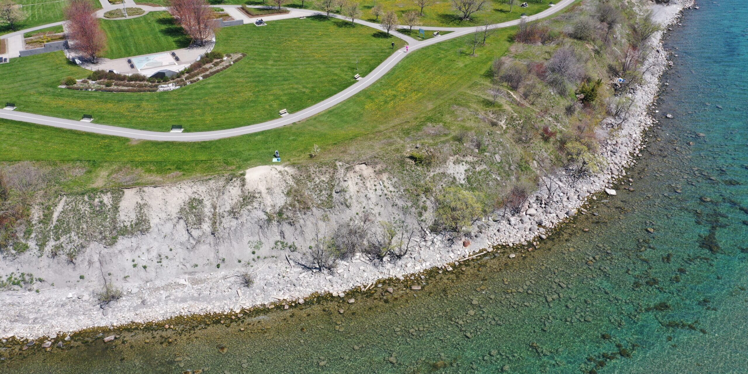 An aerial image of the shoreline around Veteran's Point Gardens showing a naturally occuring cobble beach on the right side. Stones of various size comprise the shoreline area.